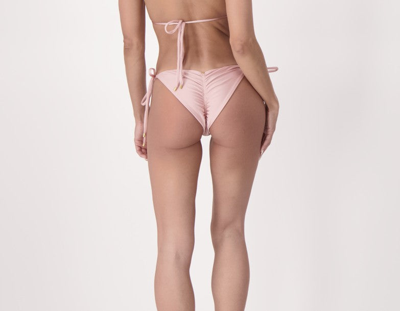 Model wearing high-quality  luxury soft pink side-tie bikini bottom with sculpted fit and a genuine Colombian emerald detail from Agua Y Amor